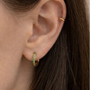 Close-up ear picture of a woman wearing a pair of emerald huggie earring