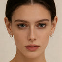 Picture of a woman wearing emerald huggie earrings with a gold chain