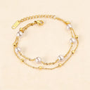 close up look of 18k gold plated bracelet with pearl charms, laying flat on beige color background
