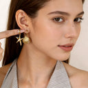 a woman holding seashell and starfish huggies on her finger close her ear 